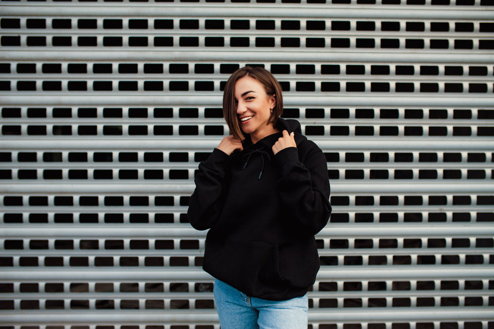 Mulher jovem e sorridente vestindo um moletom feminino preto com capuz.